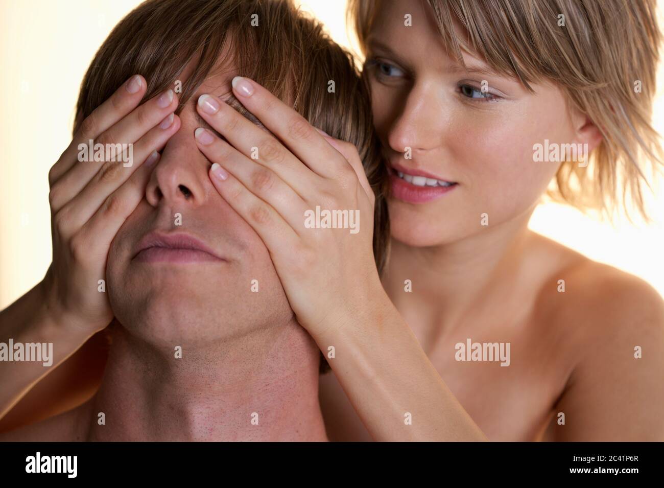 Young woman covers young man's eyes Stock Photo