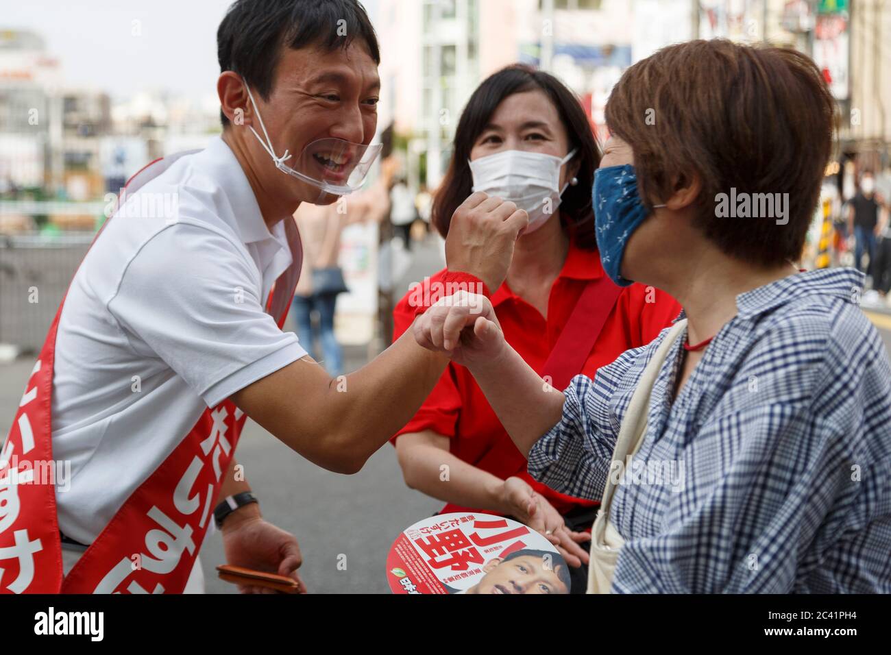 Tokyo, Japan. 23rd June, 2020. Candidate Taisuke Ono wearing a mouth shield greets voters with an elbow bump during his campaign for the Tokyo gubernatorial election outside Shimokitazawa Station. Ono, former vice governor of Kumamoto Prefecture, is campaigning for the Tokyo gubernatorial election, which will be held on July 5. Credit: Rodrigo Reyes Marin/ZUMA Wire/Alamy Live News Stock Photo