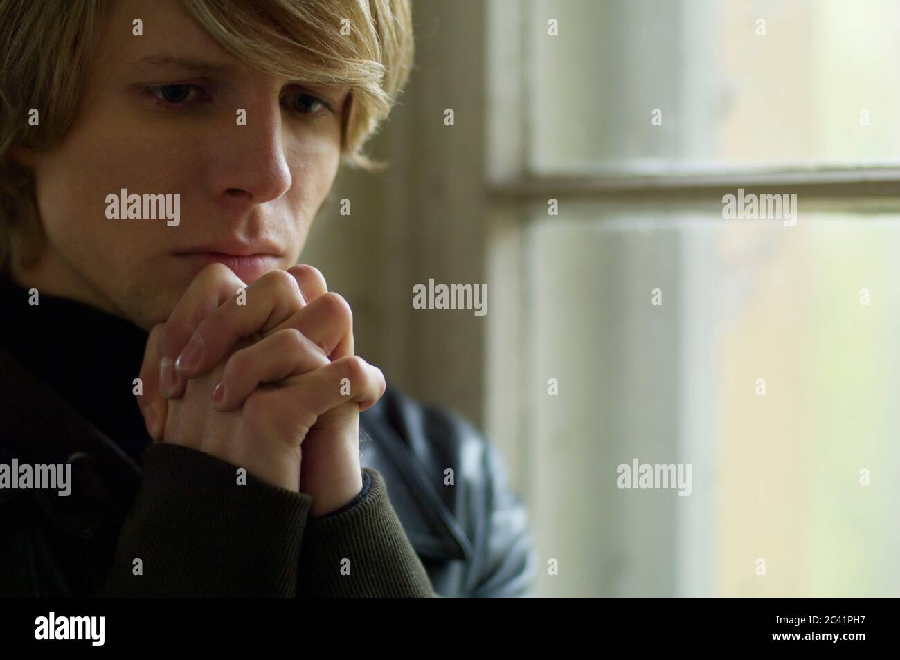 Thoughtful young man with praying hands Stock Photo
