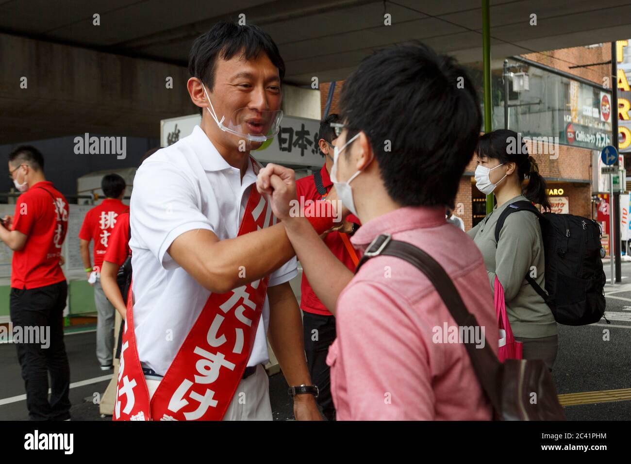 Tokyo, Japan. 23rd June, 2020. Candidate Taisuke Ono wearing a mouth shield greets voters with an elbow bump during his campaign for the Tokyo gubernatorial election outside Shimokitazawa Station. Ono, former vice governor of Kumamoto Prefecture, is campaigning for the Tokyo gubernatorial election, which will be held on July 5. Credit: Rodrigo Reyes Marin/ZUMA Wire/Alamy Live News Stock Photo