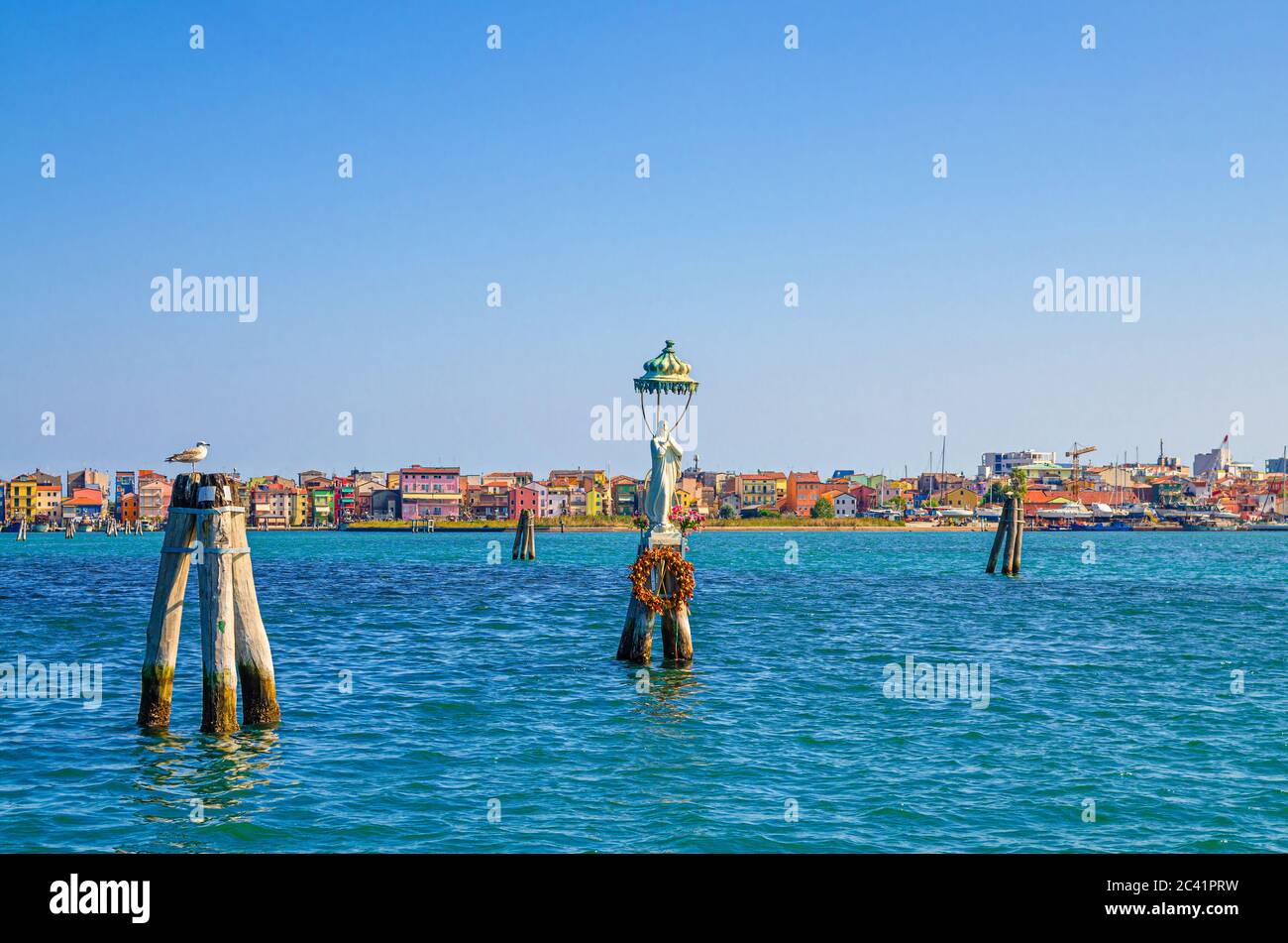 Panoramic view of Lusenzo lagoon with wooden bricole poles in water and Sottomarina town cityscape with colorful multicolored buildings, blue sky in summer day, Veneto Region, Northern Italy Stock Photo