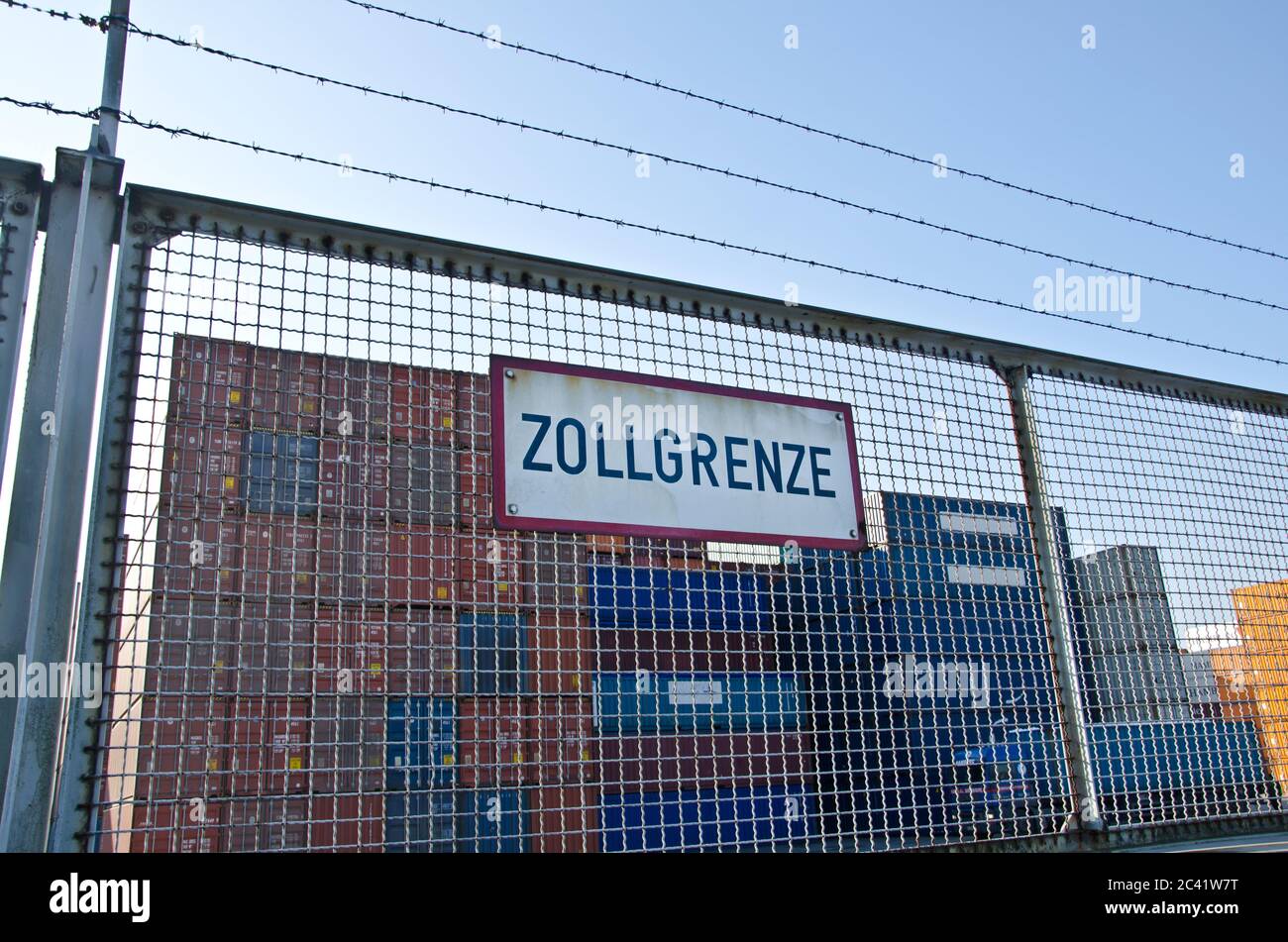 Fence in front of container harbour with sign indicating customs barrier (in German caption ‘Zollgrenze’) Stock Photo