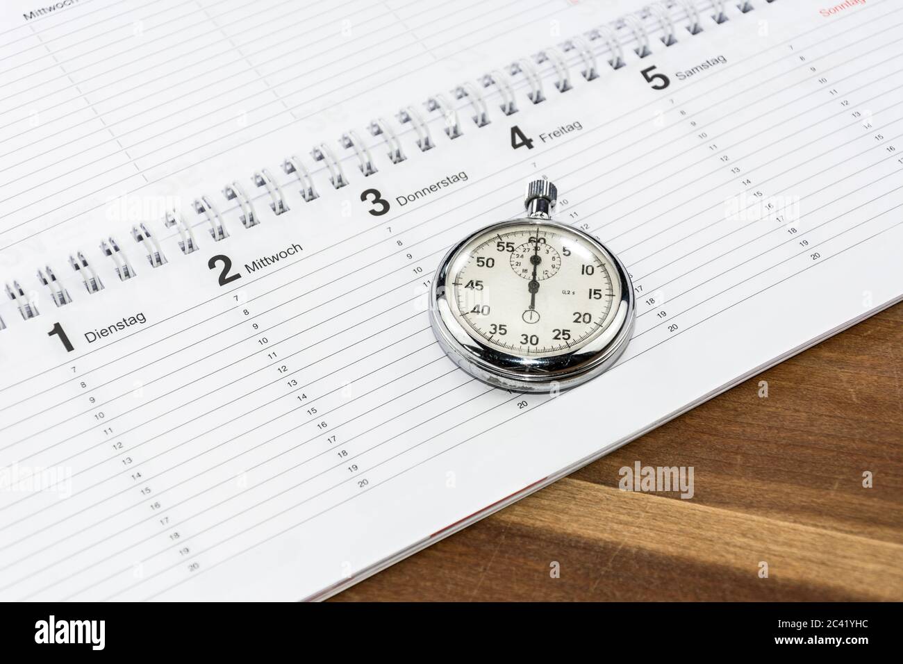 Stopwatch lying on a schedule on a wooden desk (with captions of the days of the week in German) Stock Photo