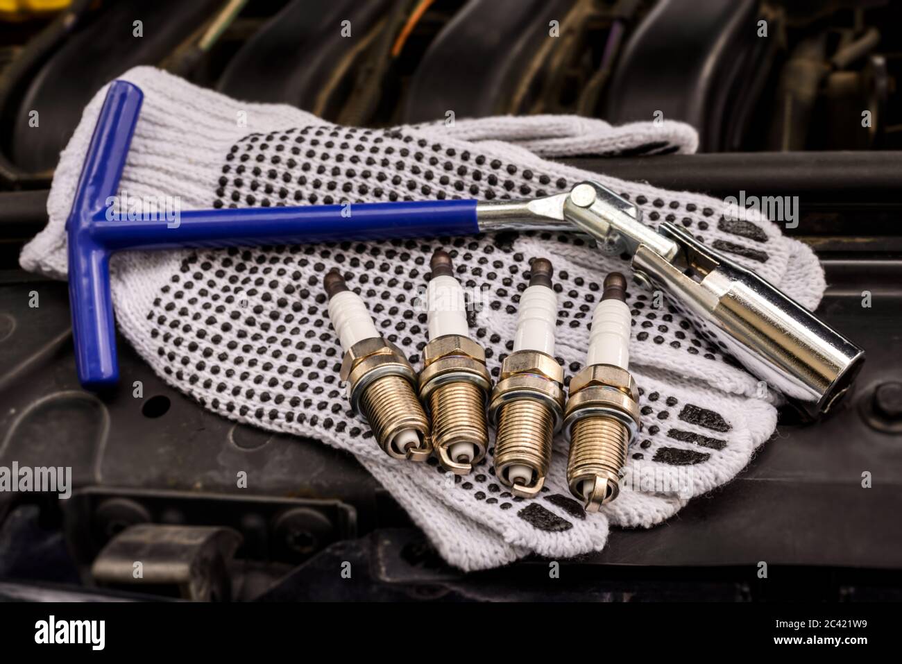 Sparking plugs, spark plug key and protective gloves under the hood of the car. Stock Photo