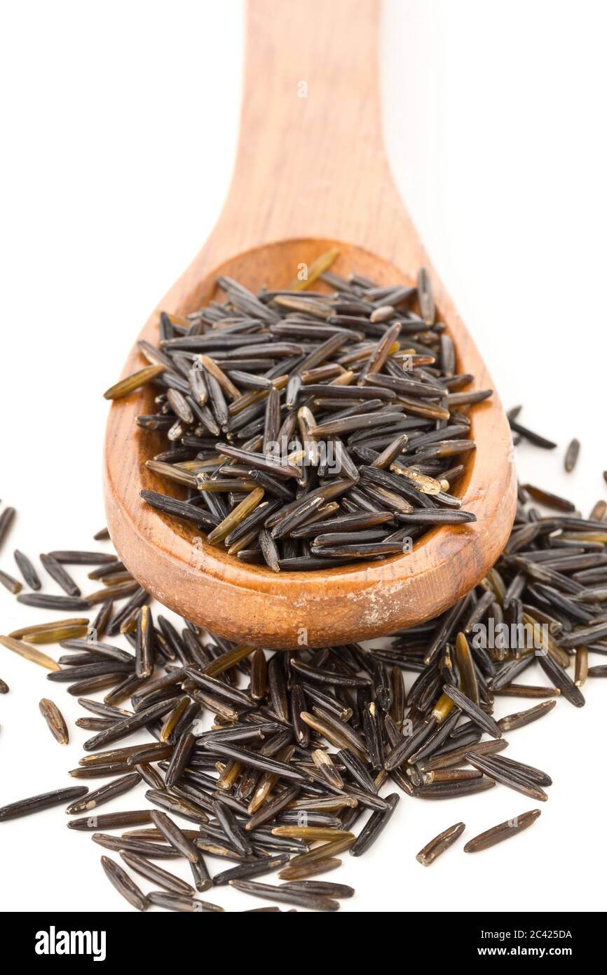 Heap of uncooked, raw, black wild rice grains in wooden spoon over white background, selective focus Stock Photo