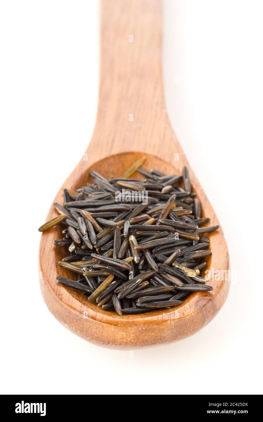Heap of uncooked, raw, black wild rice grains in wooden spoon over white background, selective focus Stock Photo