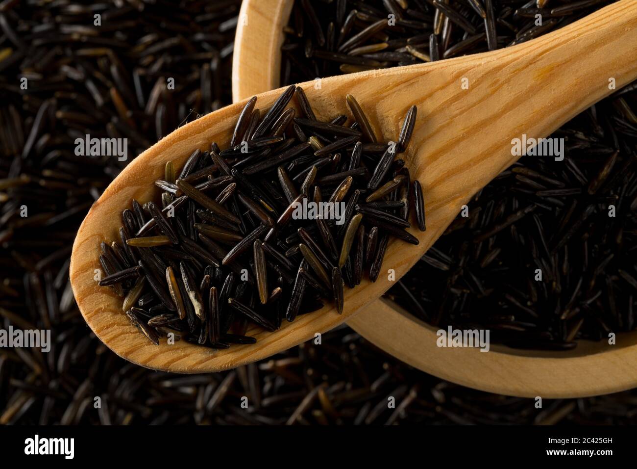 Heap of uncooked, raw, black wild rice grains in wooden scoop and wood bowl on rice grain background, selective focus, flat lay top view from above Stock Photo