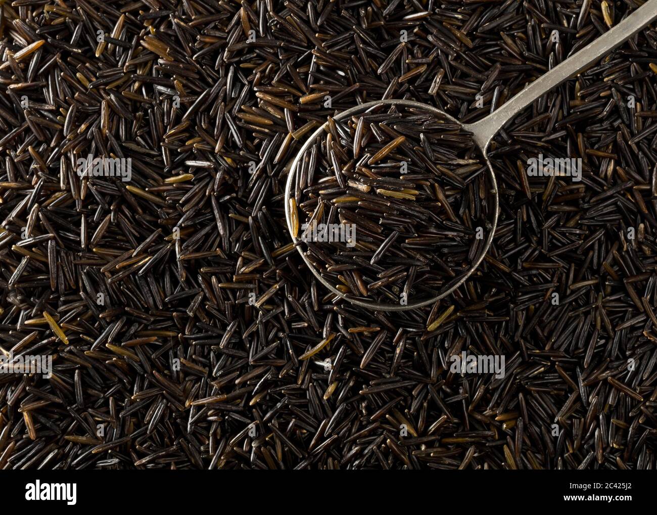 Heap of uncooked, raw, black wild rice grains in metal scoop on rice grain background, selective focus, flat lay top view from above Stock Photo