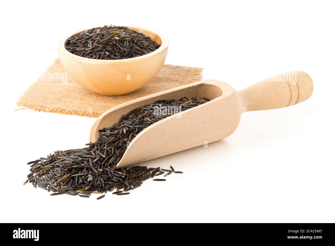 Heap of uncooked, raw, black wild rice grains in wooden scoop and wood bowl over white background, selective focus Stock Photo