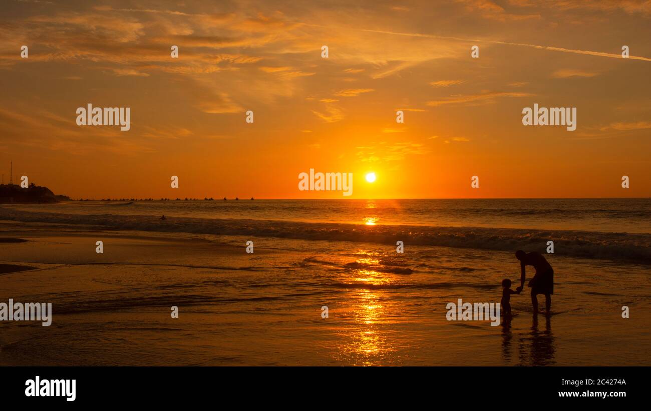 Dad with his daughter playing on the beach at sunset with the sun shine reflecting in the sea Stock Photo