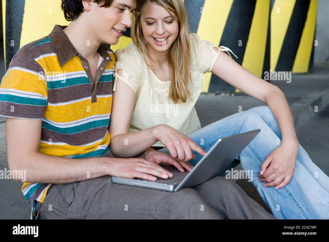 Young couple sitting with a laptop in front of striped pillars - garage - relationship Stock Photo