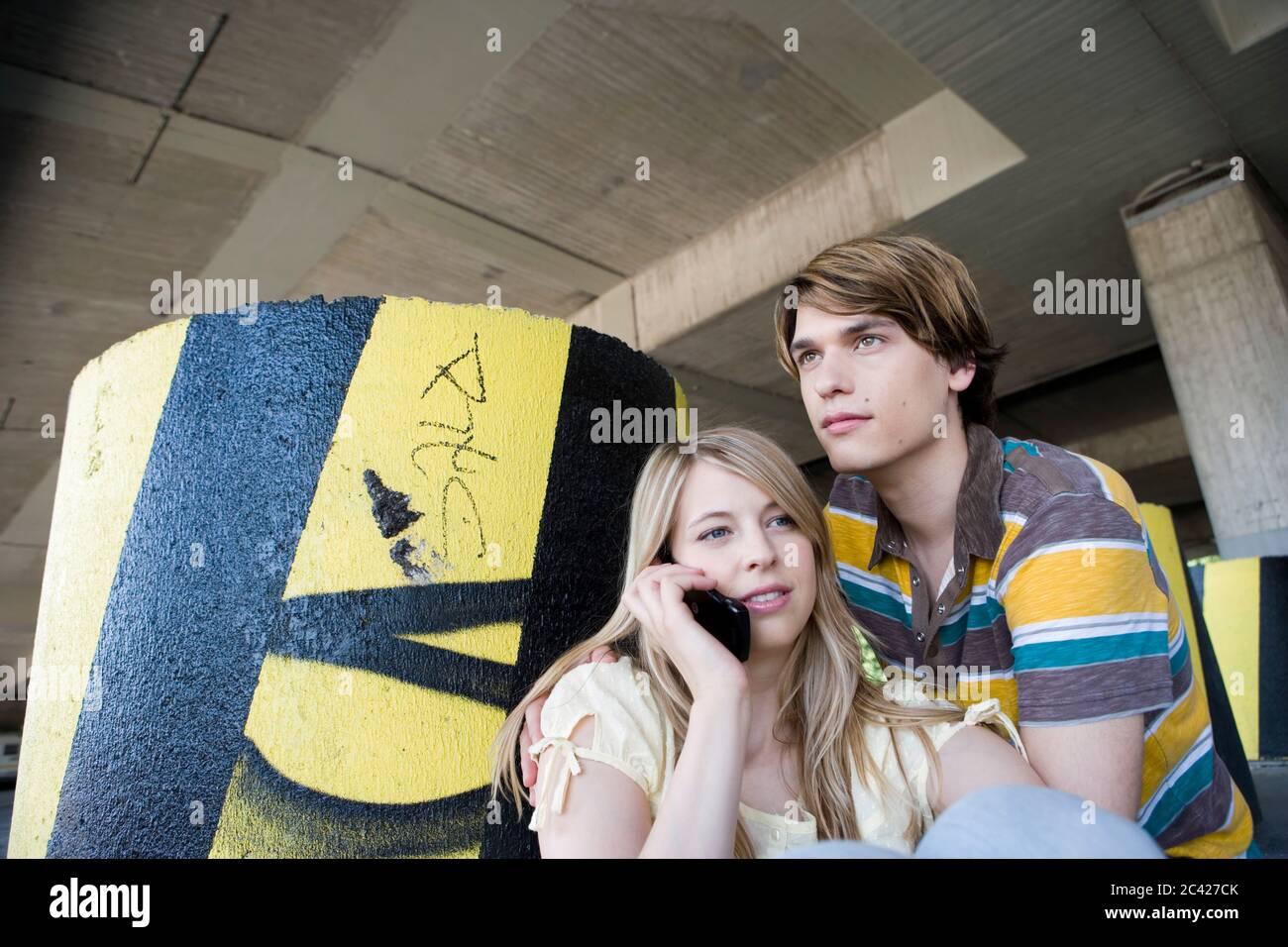 Young brunette man in a striped shirt behind a blonde woman who is on the phone - youth relationship Stock Photo