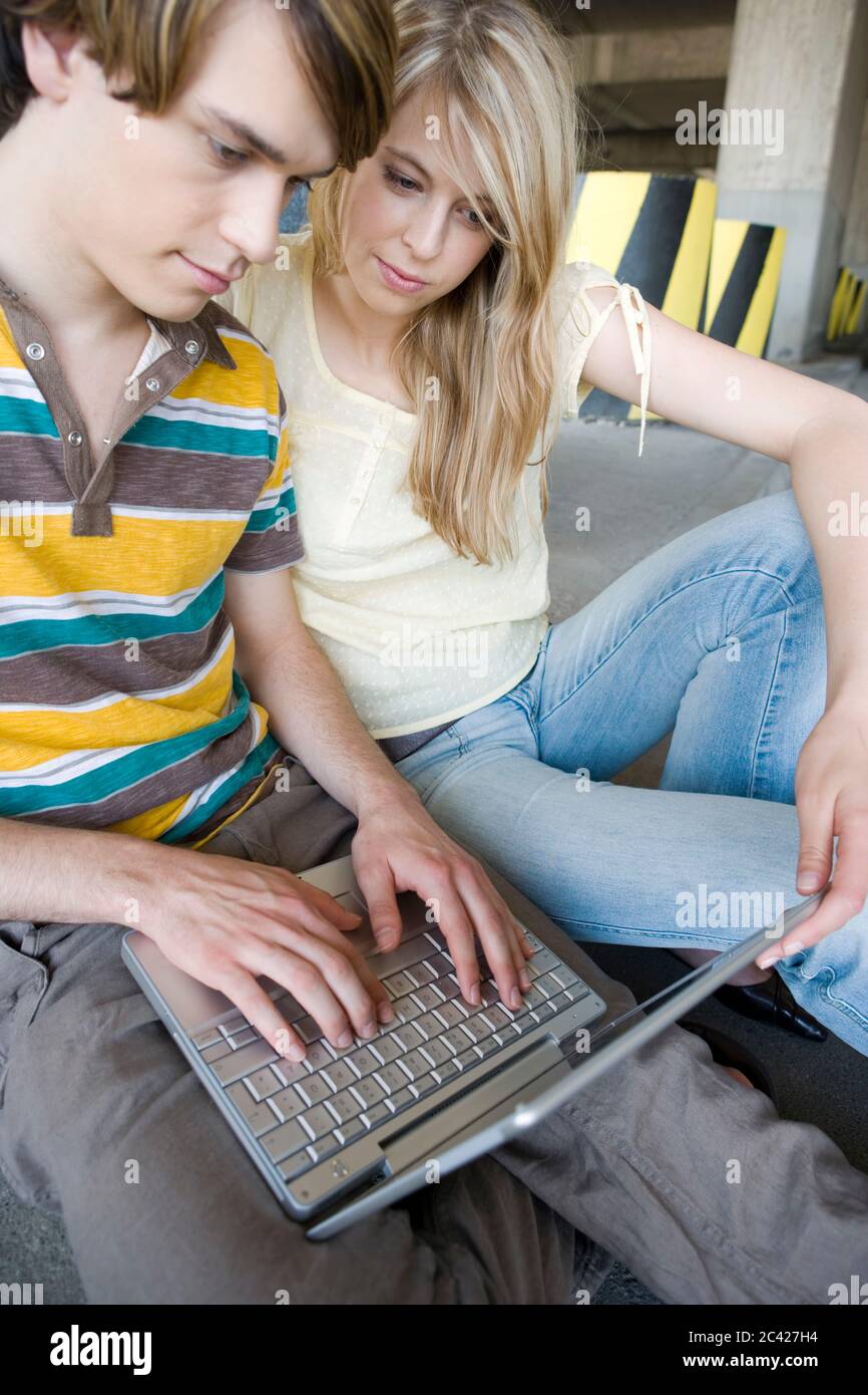 Young couple sitting with a laptop in front of striped pillars - garage - relationship Stock Photo