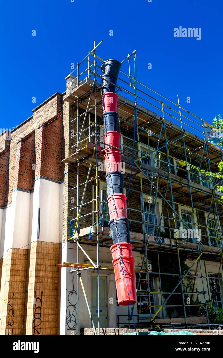 Red and black construction trash chute used during a house renovation, scaffolding on house facade Stock Photo