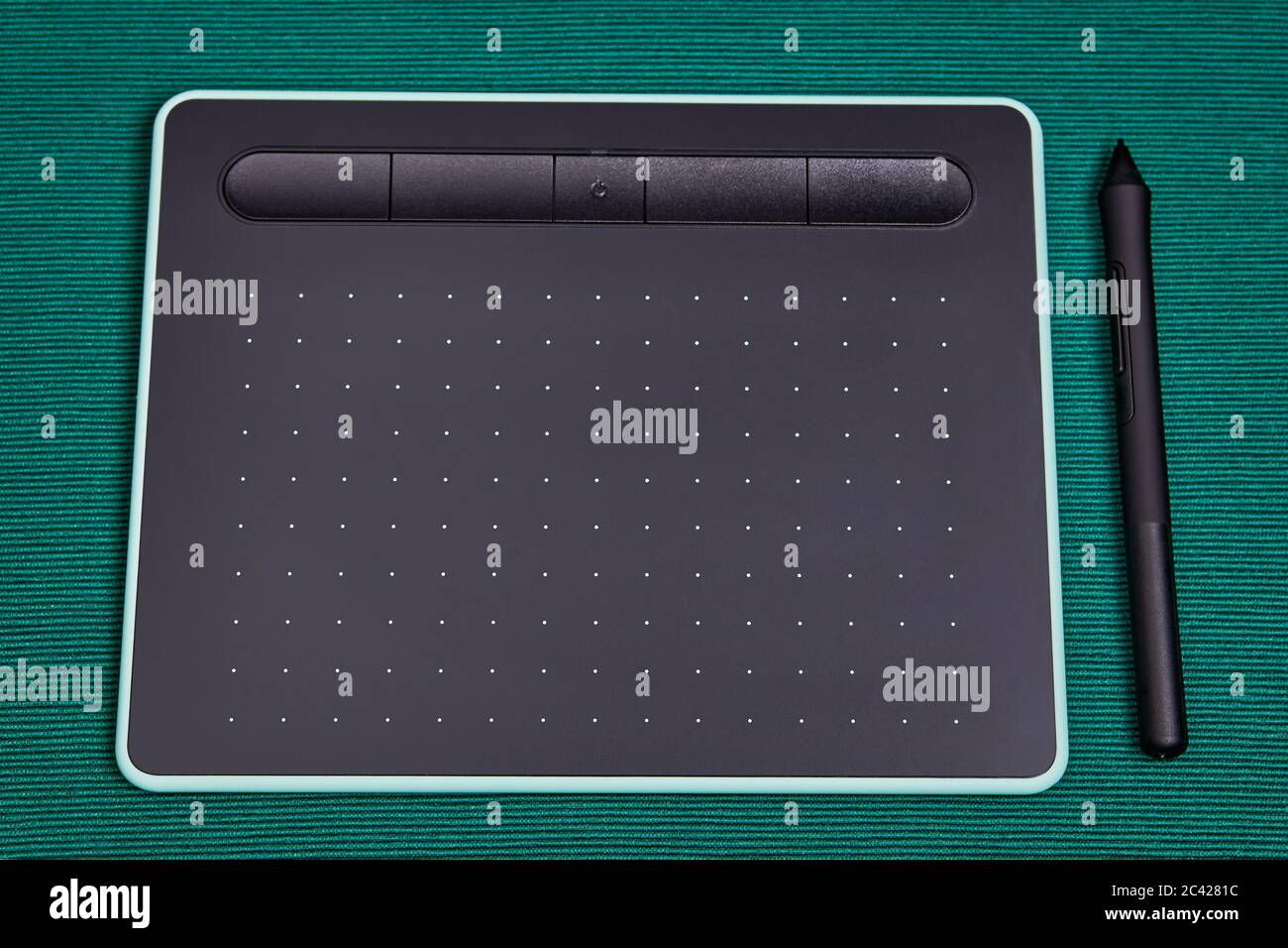 An electronic input device for a personal computer, a graphic tablet with a stylus pen, lies on a table covered with a green cloth. Drawing board for Stock Photo