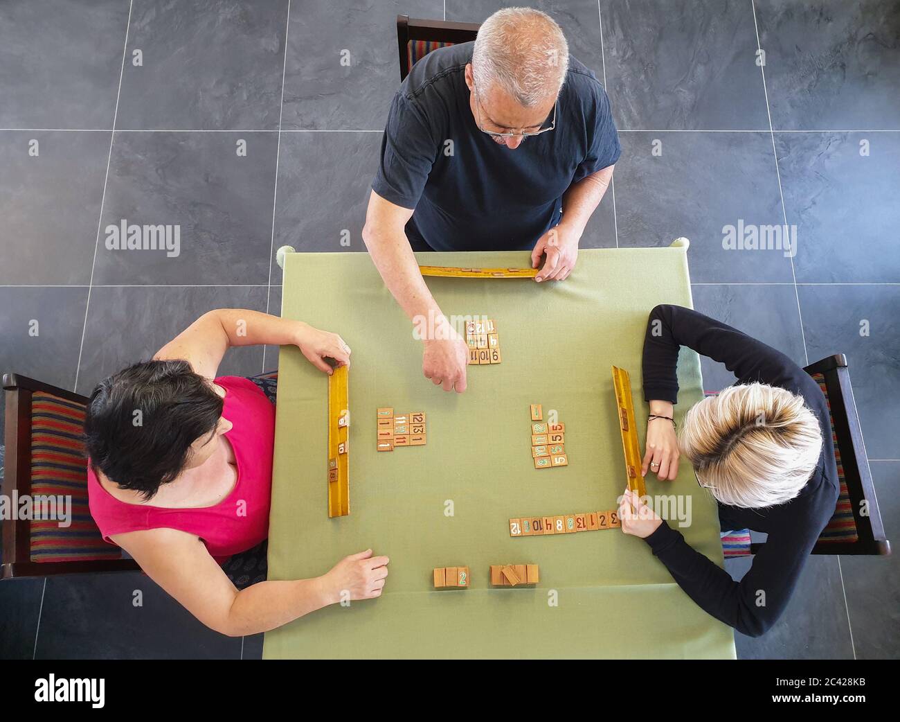 Family of three playing rummy game on table inside. Indoor home isolation activity, as social distancing quarantine measures restrict going outside du Stock Photo