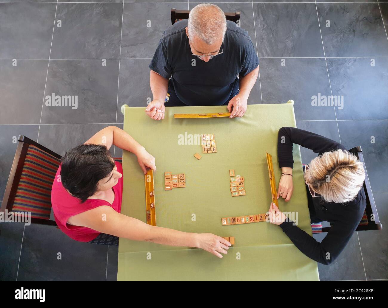 Family of three playing rummy game on table inside. Indoor home isolation activity, as social distancing quarantine measures restrict going outside du Stock Photo