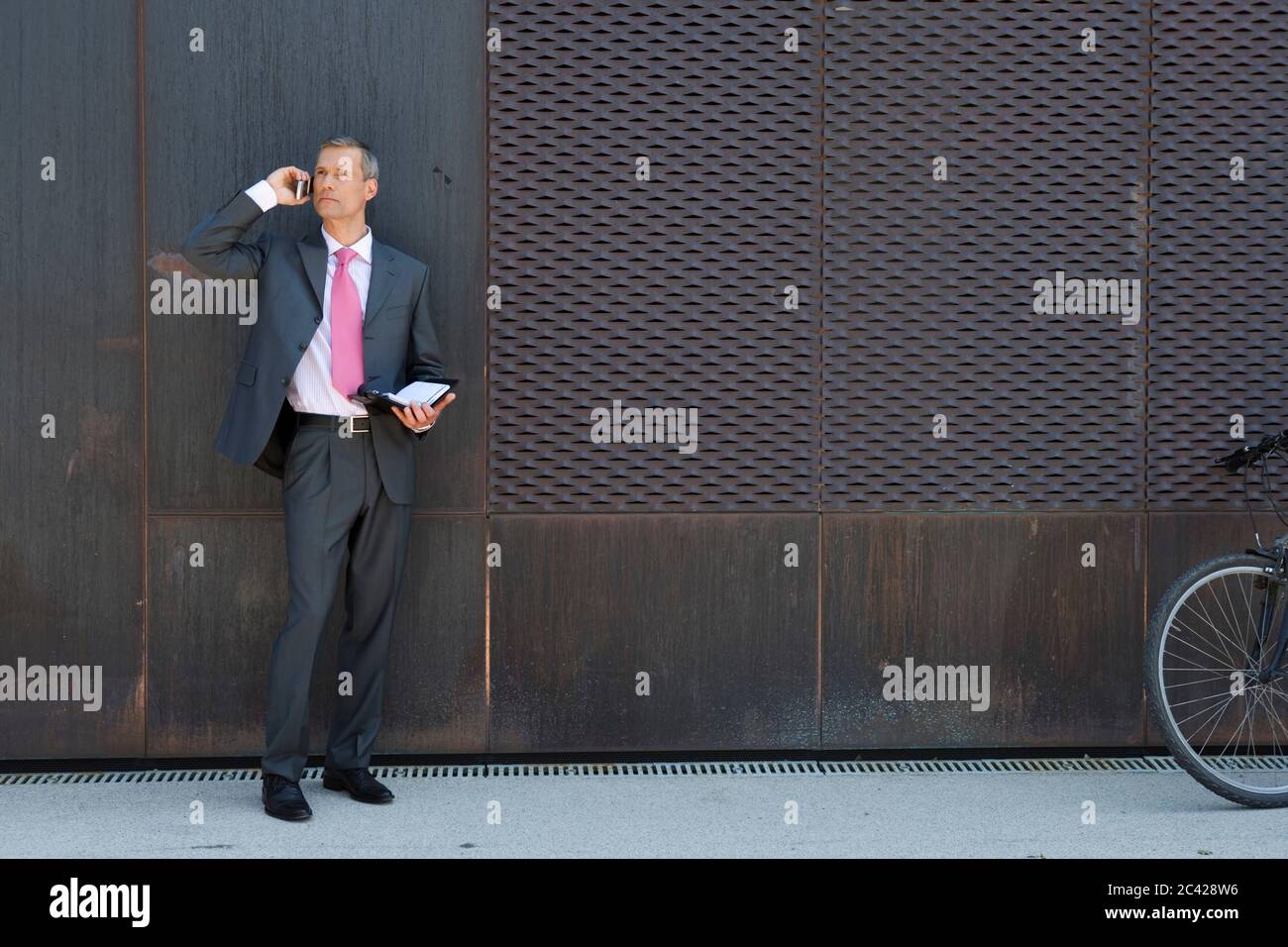 Businessman stands in front of a garage entrance and uses a mobile phone to communicate Stock Photo