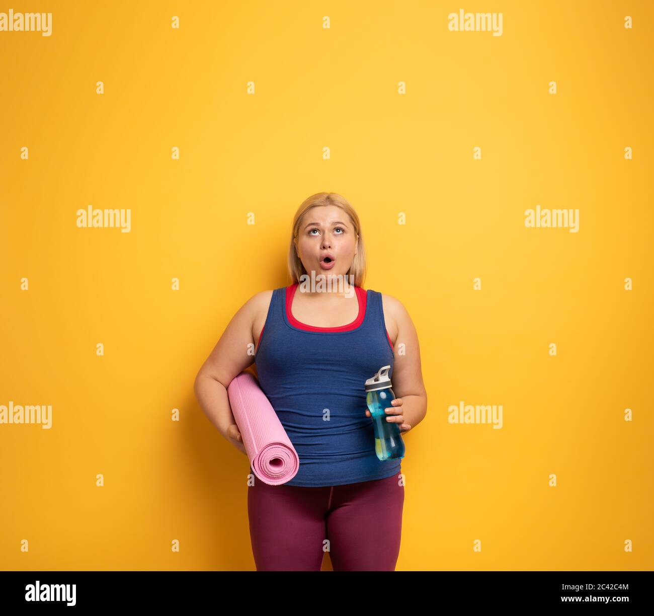 Fat girl does gym at home. surprised expression. Yellow background Stock Photo