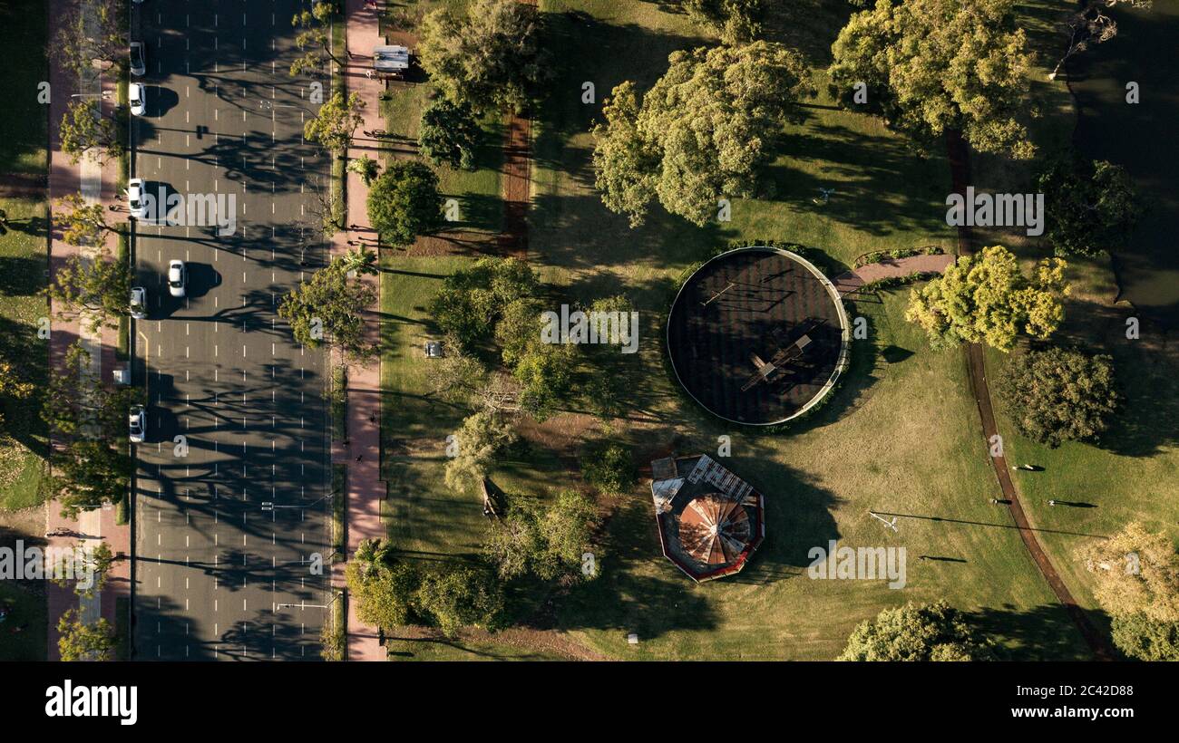 Aerial top-down view on the public park with rounded plaza with playground area with the avenue and cyclist path by the side during the sunset. Stock Photo