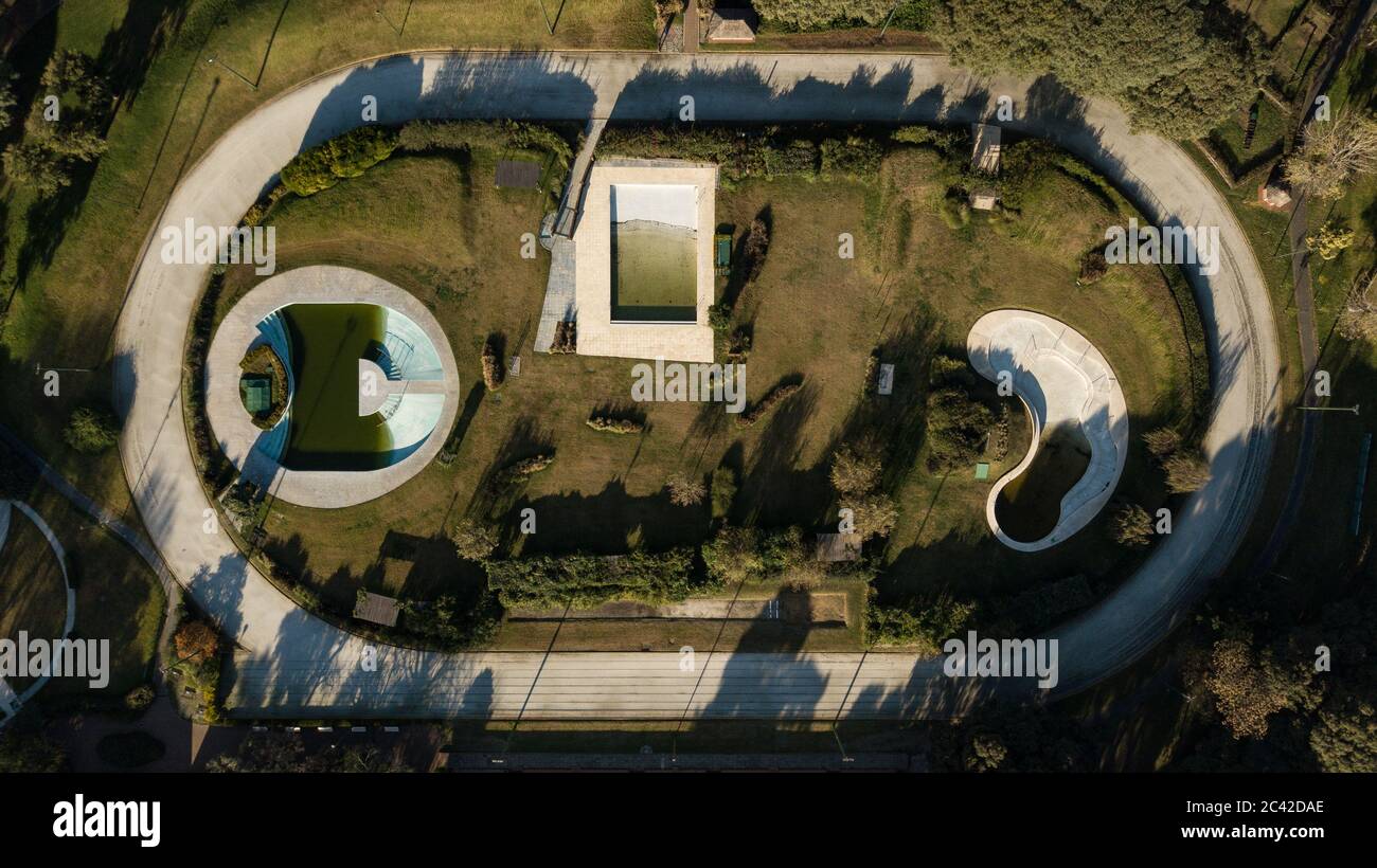 Aerial top-down view on sports field filled with different shapes swimming pools half-filled with water, surrounded by green grass, plants and trees. Stock Photo