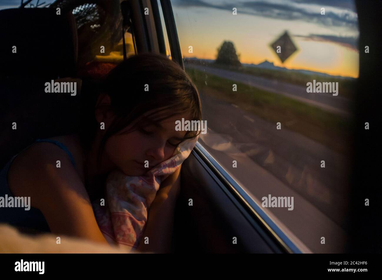 A young girl sleeping in the back of a car with her head on the window Stock Photo
