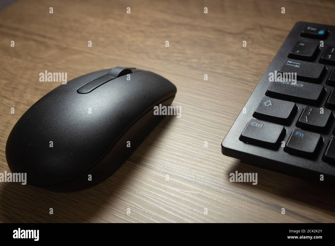 Wireless mouse and keyboard set on top of a wooden office desk, on a