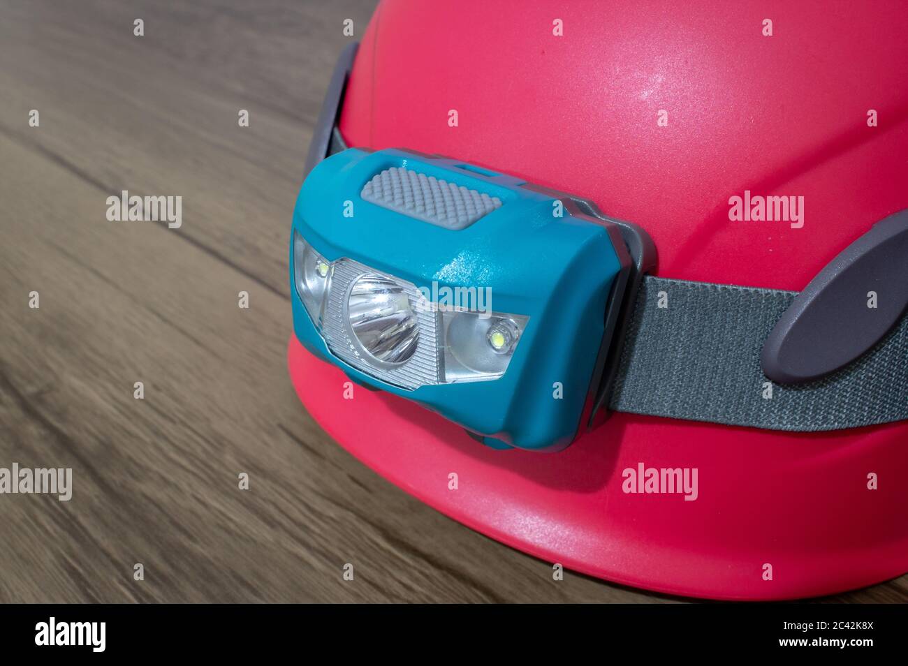 Teal led headlamp turned off strapped to a pink climbing helmet on a wooden table Stock Photo