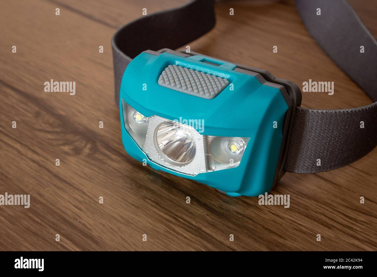 Teal led headlamp turned off on a wooden table showing the elastic strap Stock Photo
