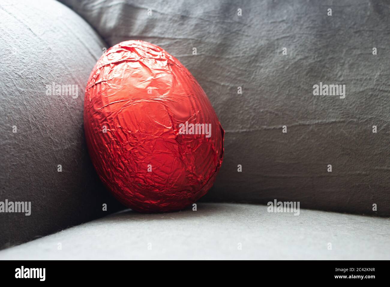 Red easter egg on the corner of a couch still unwrapped Stock Photo