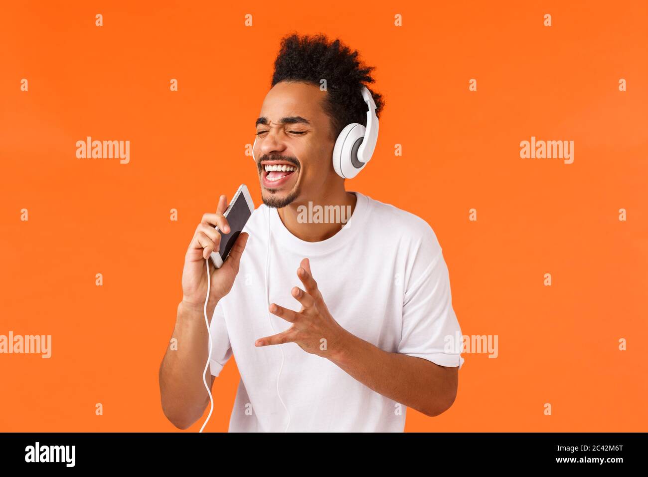 Passionate and carefree african-american guy dreaming become real singer, holding smartphone and singing into mobile phone as playing karaoke app Stock Photo