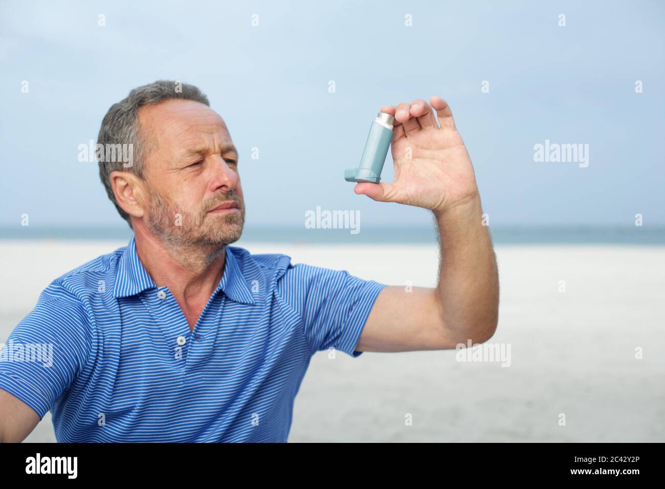 Middle-aged man using an inhaler on the beach Stock Photo