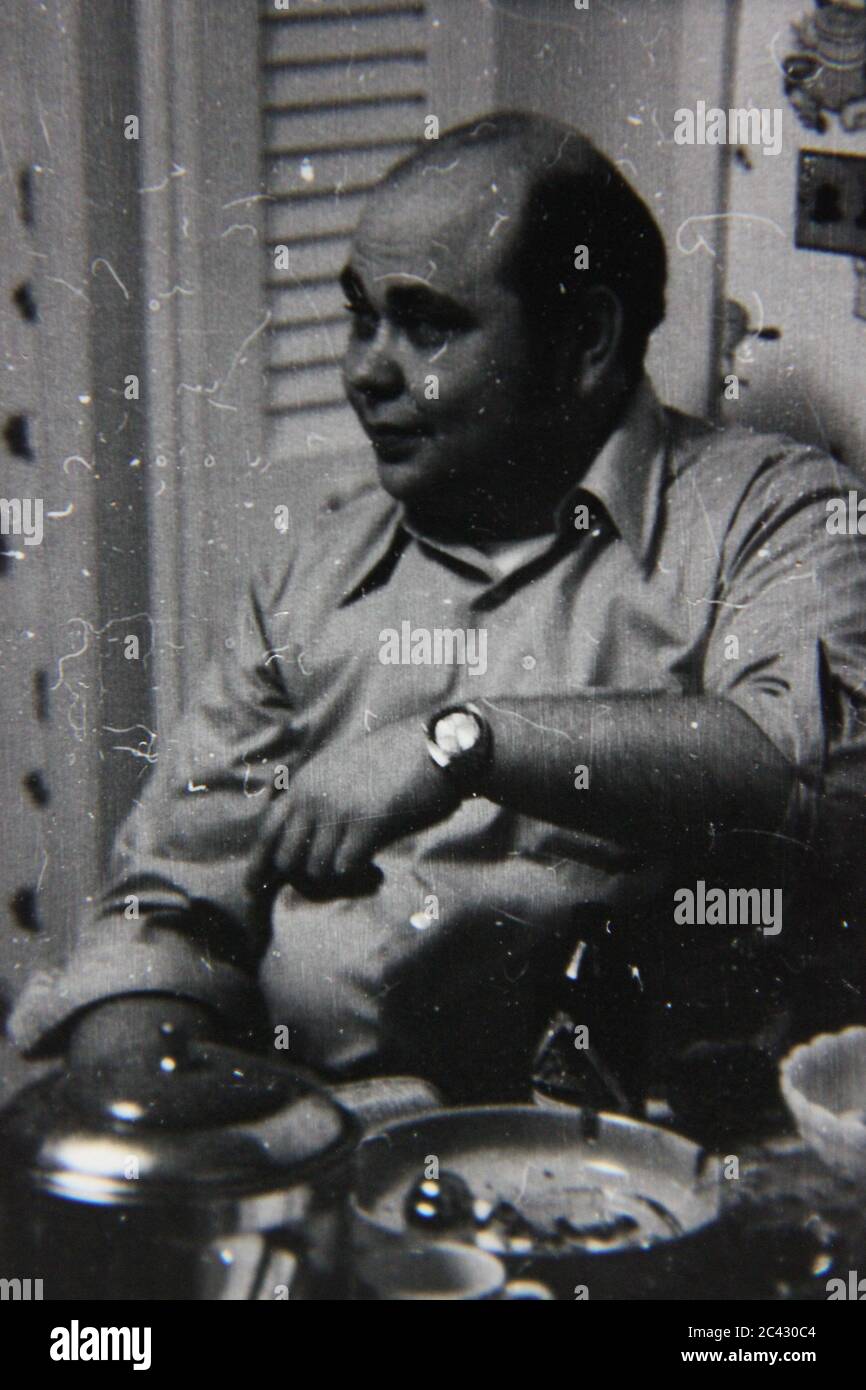 Fine 70s vintage black and white lifestyle photography of a thirty something balding man hanging out in the kitchen. Stock Photo