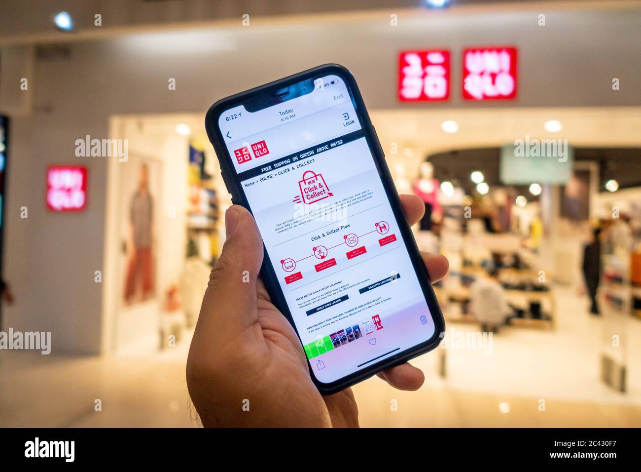 A man's hand holding an iphone X with uniqlo apps infront of Uniqlo store.  Uniqlo apps is perfect for those who prefer online shopping Stock Photo -  Alamy