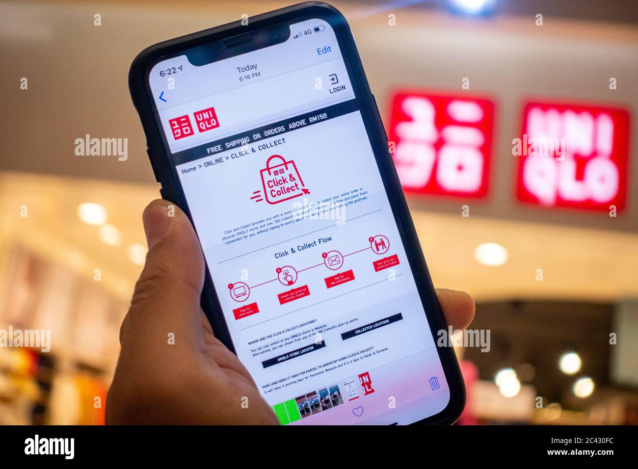 A man's hand holding an iphone X with uniqlo apps infront of Uniqlo store.  Uniqlo apps is perfect for those who prefer online shopping Stock Photo -  Alamy