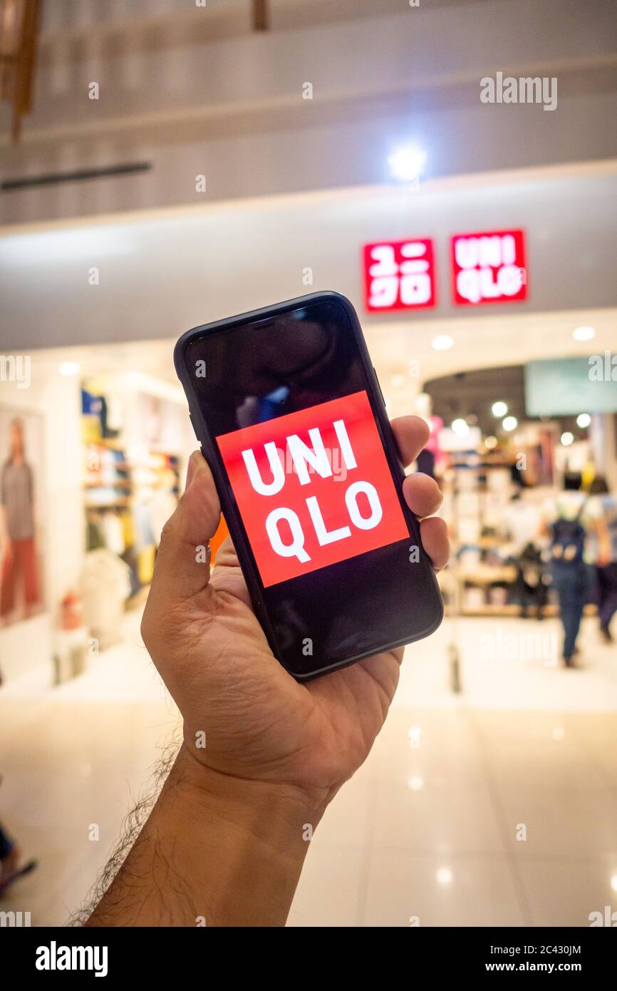 A man's hand holding an iphone X with uniqlo apps infront of Uniqlo store.  Uniqlo apps is perfect for those who prefer online shopping Stock Photo -  Alamy