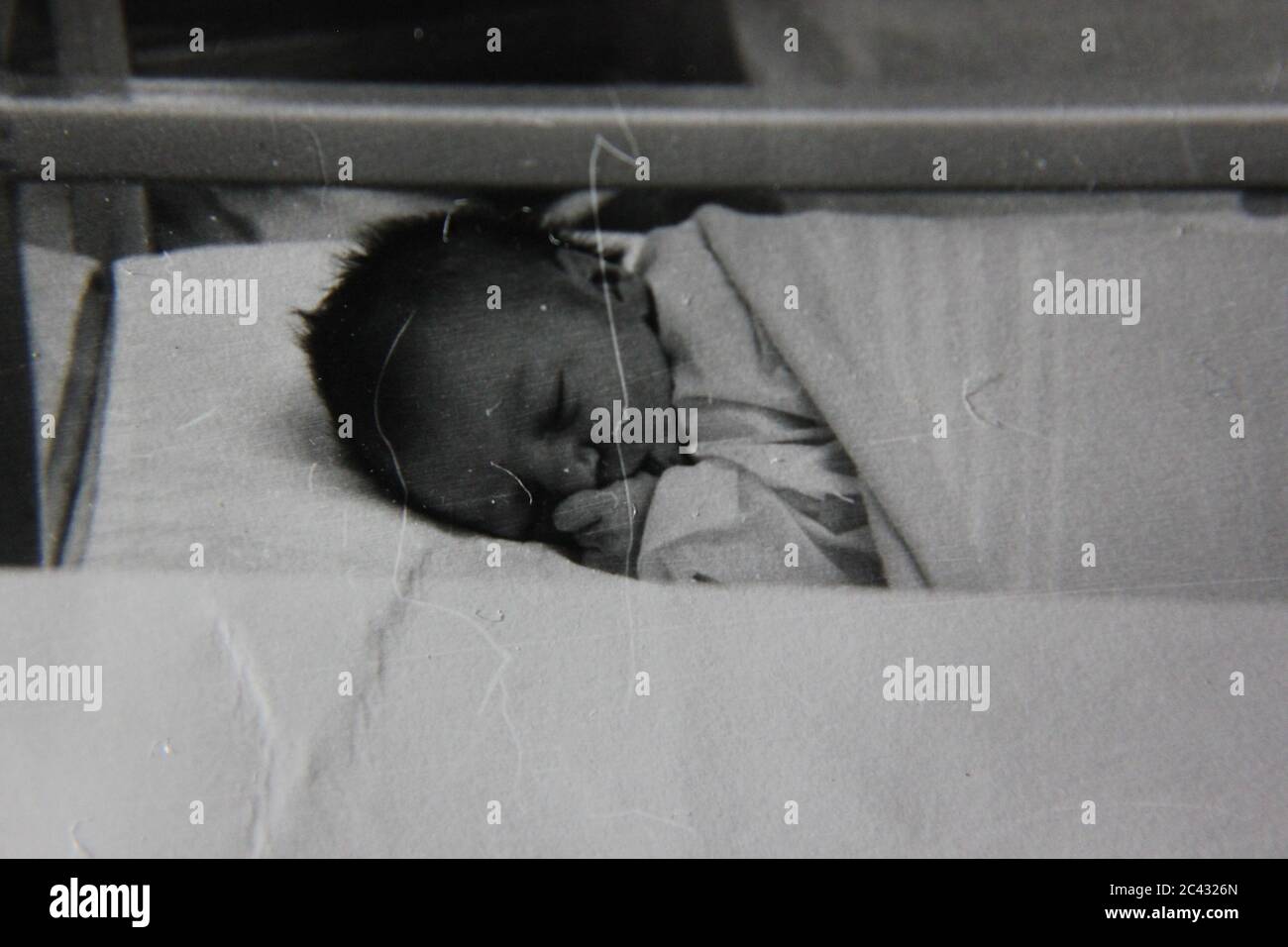 Fine 1970s black and white photography of a newborn baby in the hospital maternity ward trying to sleep in its crib. Stock Photo