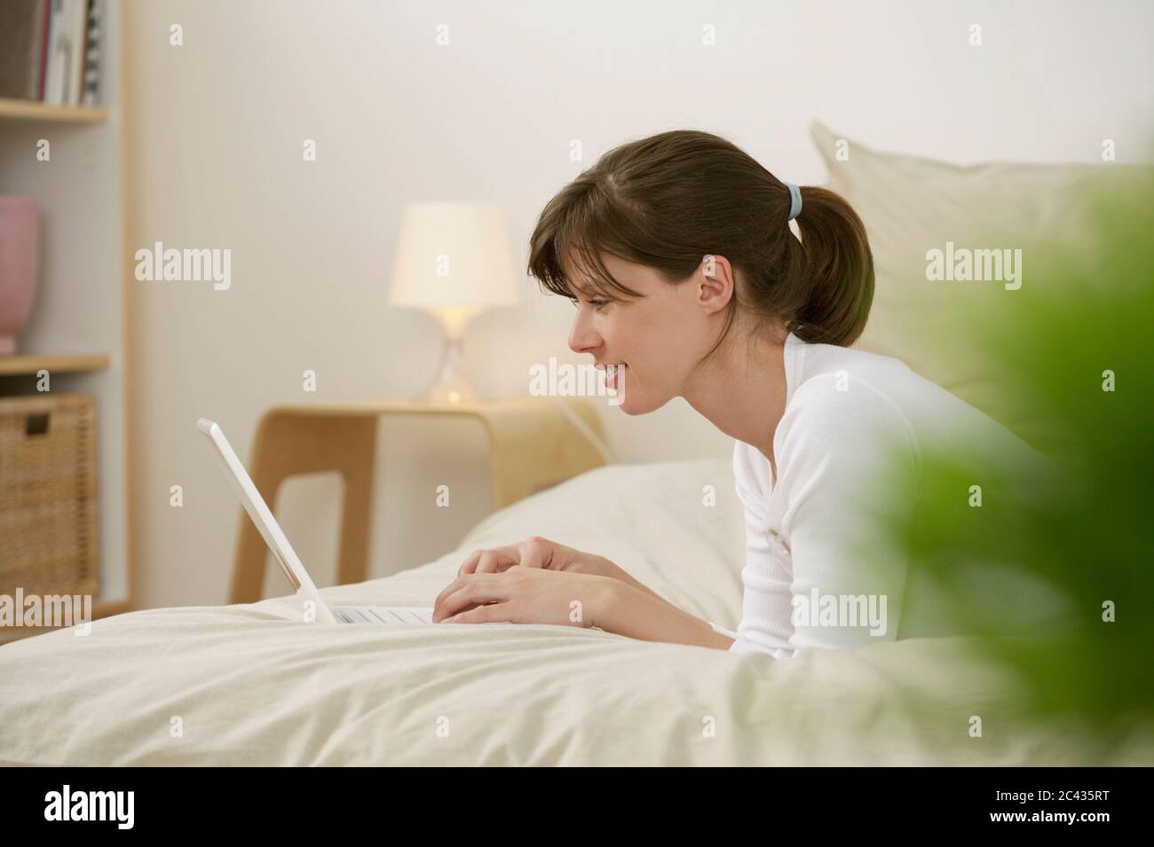Woman lying on bed with laptop Stock Photo - Alamy