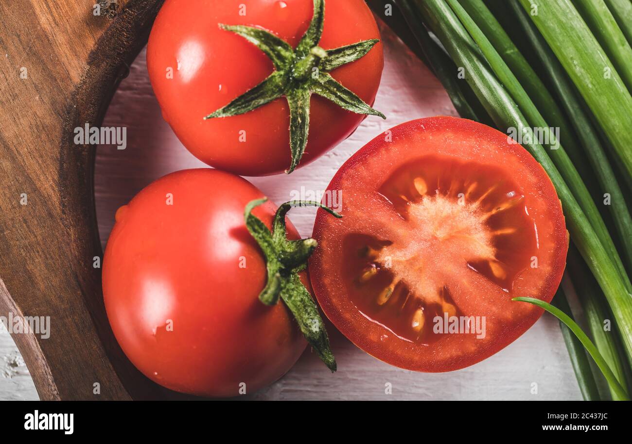Fresh whole and half cut tomatoes with green herbs around a wooden board Stock Photo