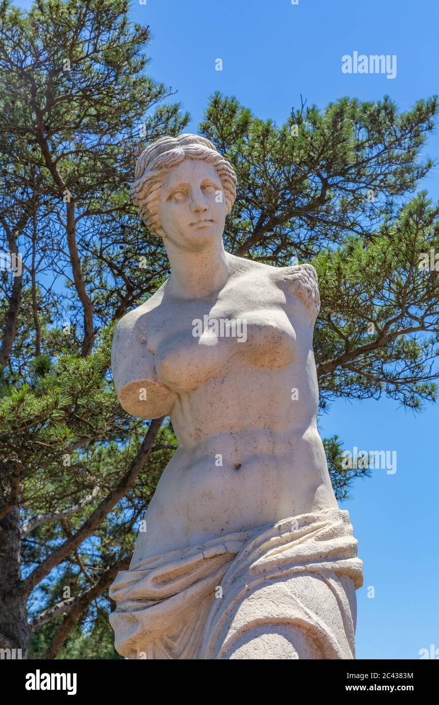 Outdoor blue sky green tree, broken arm Venus statue, Roman mythology, Aphrodite Stock Photo