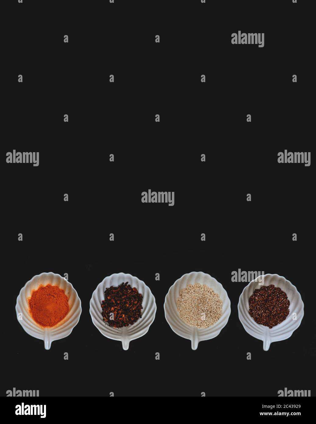 A border of spices and grains in white cups on a black isolated background. Stock Photo