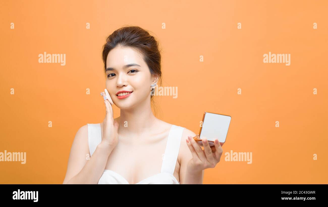 Pretty Asian girl making up or makeup her face by puff the foundation powder while looking mirror on the foundation powder puff Stock Photo