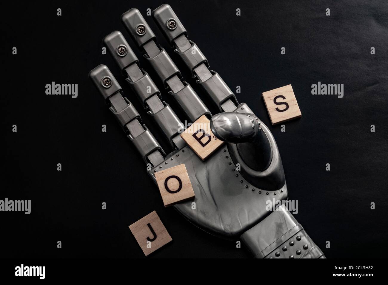 Lose your job to robots due to automation and the rise of the machines concept with a robot hand grabbing wooden tiles that spell out the word JOBS on Stock Photo