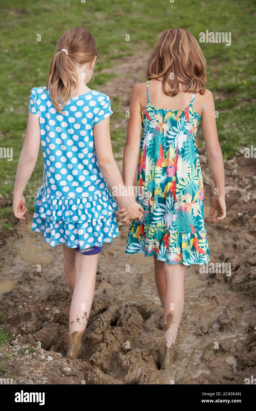 Two girls walk hand in hand through the mud, barefoot, rear view Stock Photo