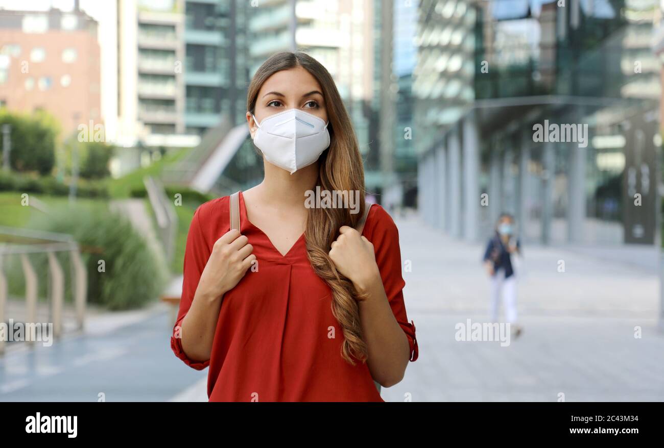 Young woman wearing protective mask KN95 FFP2 walking in modern city street. Student girl with face mask against Coronavirus Disease 2019 (COVID-19). Stock Photo