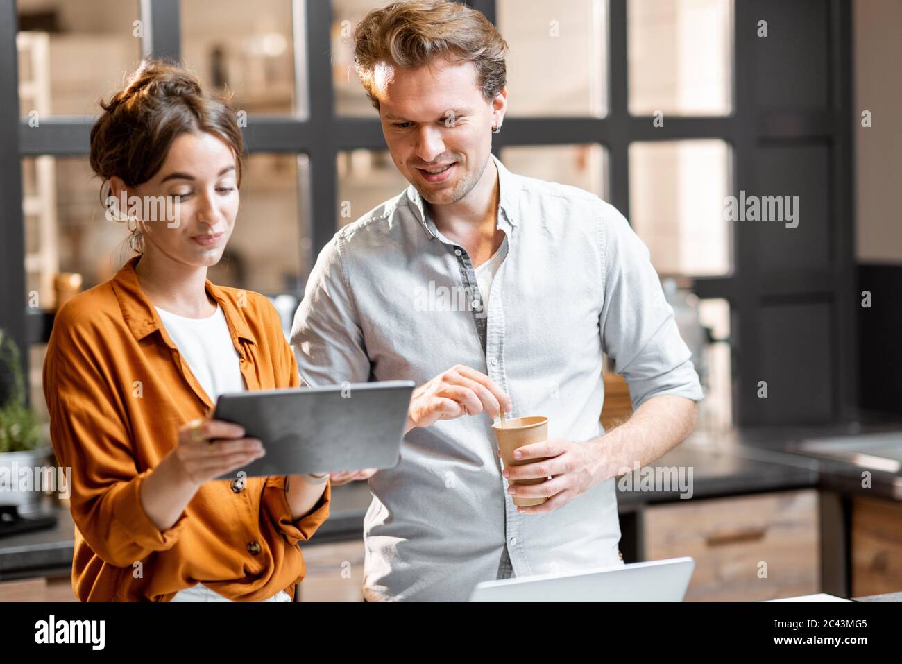 Two young managers or shop owners having some discussion while standing with a digital tablet at the counter of the shop or cafe. Small business management concept Stock Photo