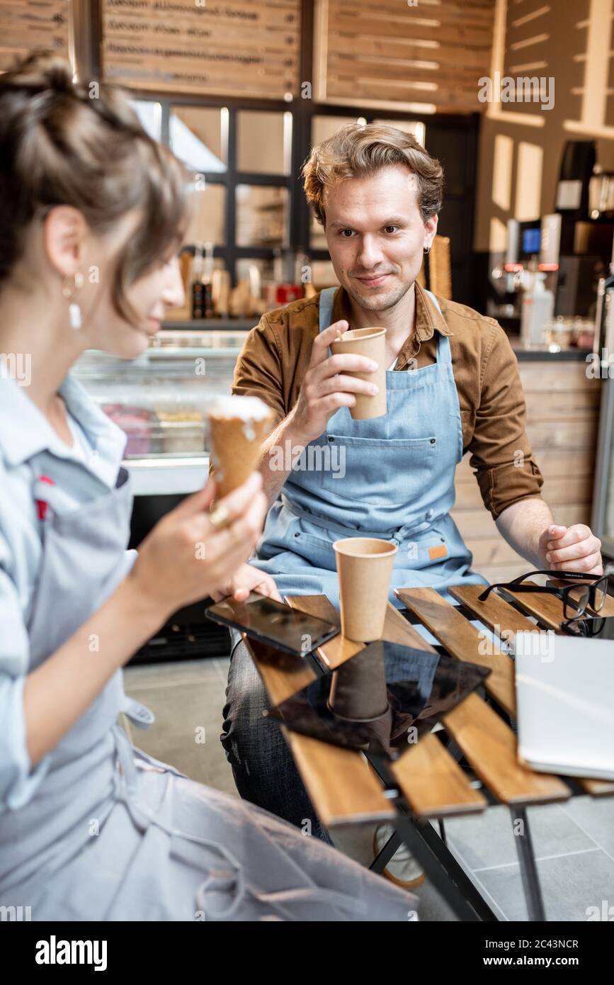 Couple of a young cafe workers have some business conversation while sitting with coffee at the table of their cafe or pastry shop Stock Photo
