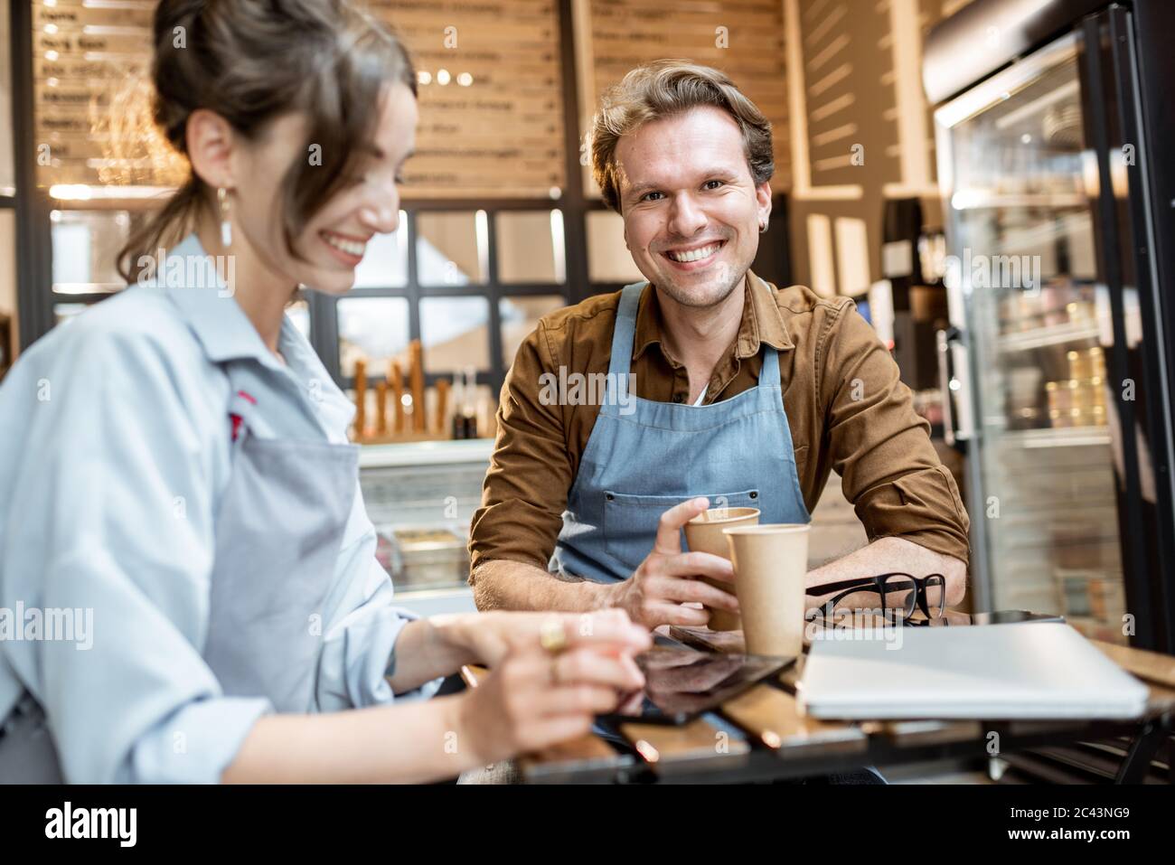 Couple of a young cafe workers have some business conversation while sitting with coffee at the table of their cafe or pastry shop Stock Photo
