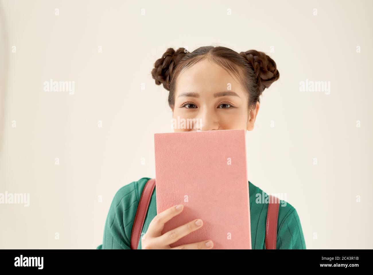 Portrait of a funny young school nerd girl holding book at her face isolated over white background Stock Photo