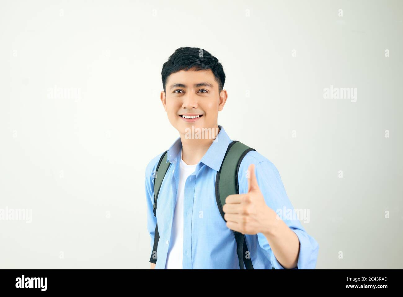 Portrait of a smiling male student with backpack showing thumbs up over ...